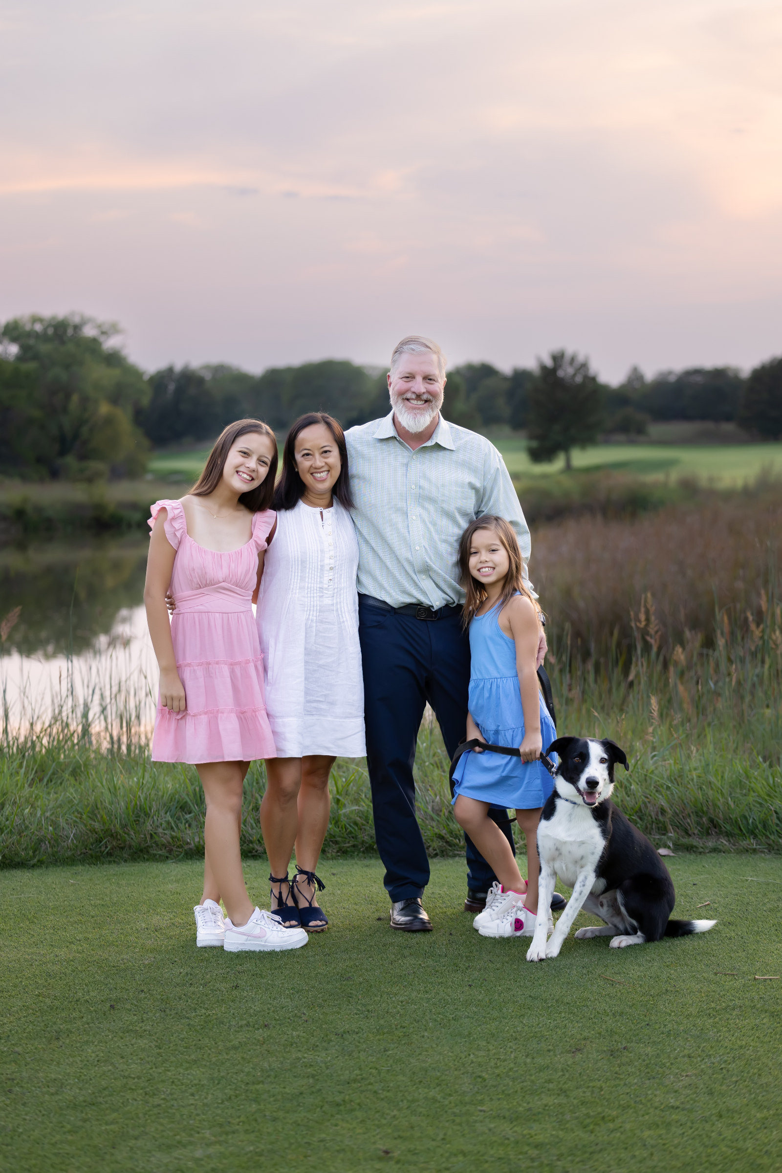 Family posing outdoors with their dog in a green field