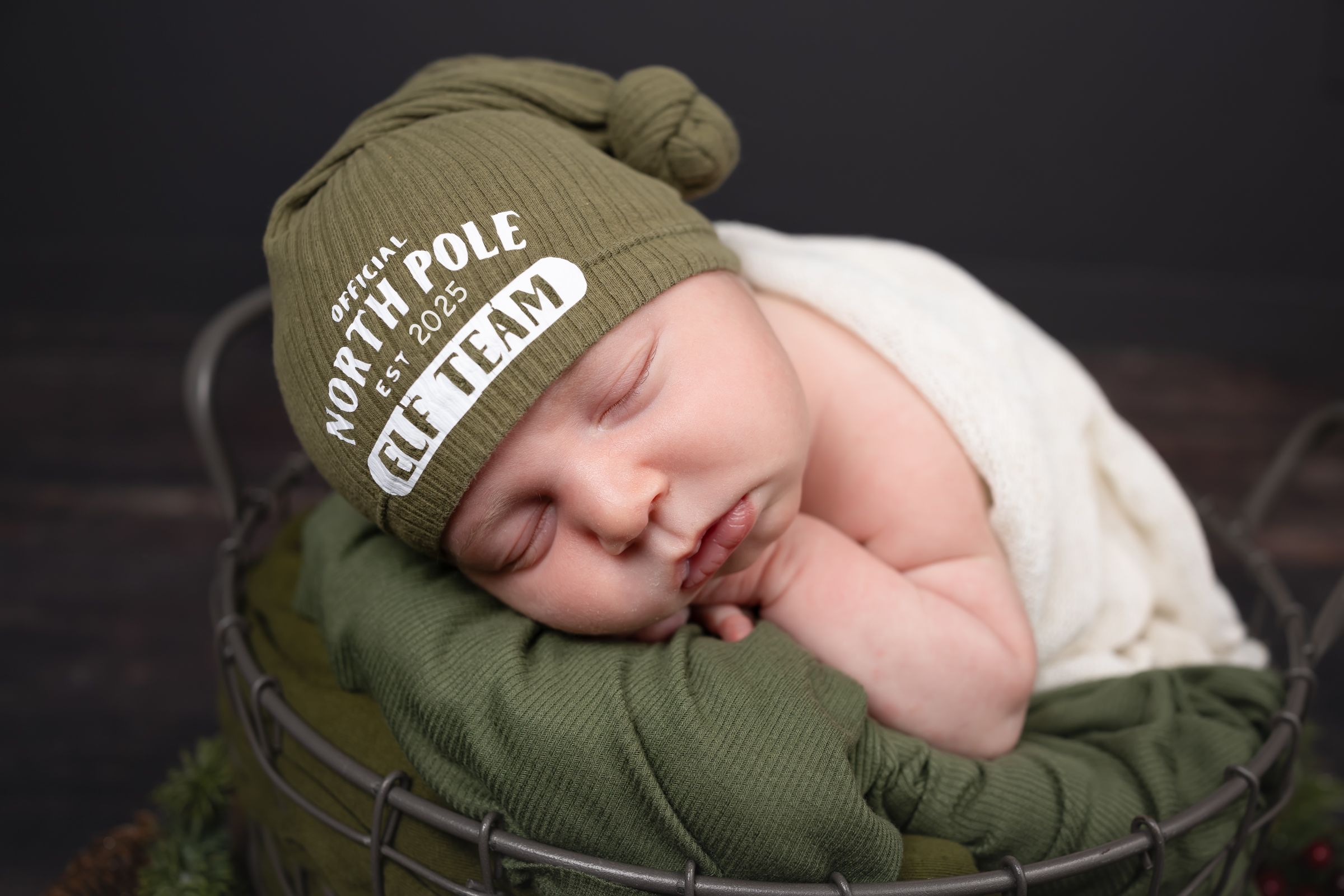 Sleeping newborn wearing an olive-green hat, curled up in a basket