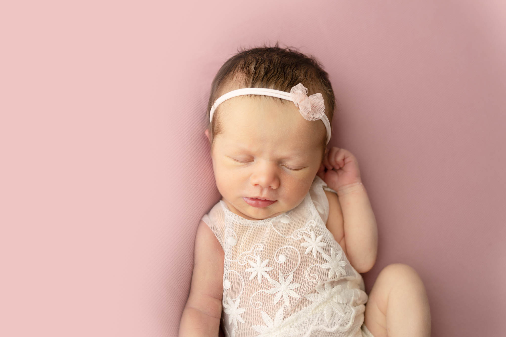 Newborn wearing a white floral outfit and pink headband